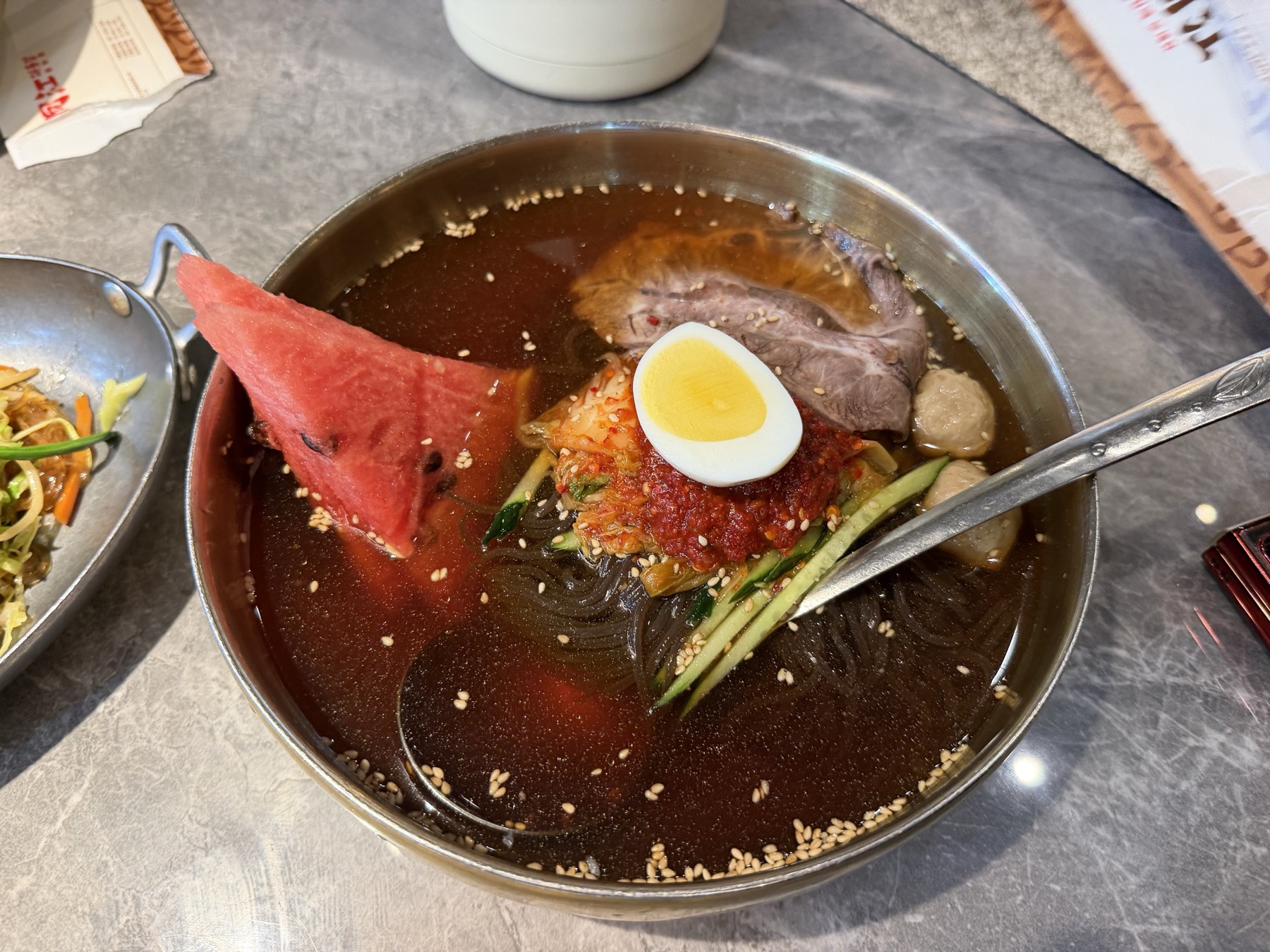 A bowl of cold noodles with egg, beef, and watermelon